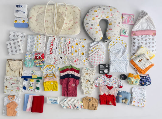 A flat lay of baby essentials and clothing items arranged neatly on a white background, including a U-shaped nursing pillow, a bassinet, folded baby clothes, socks, wipes, and small accessories. baby hospital kit chennai